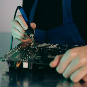 Person using a soldering iron on a printed circuit board.