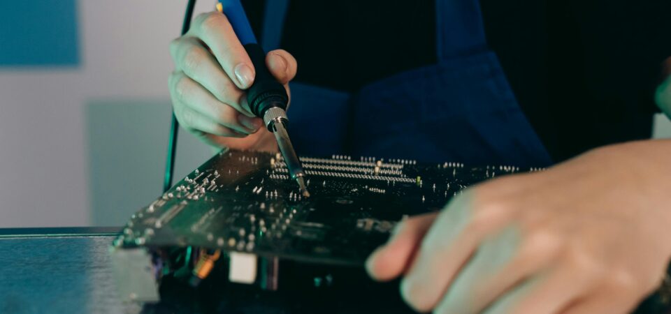 Person using a soldering iron on a printed circuit board.